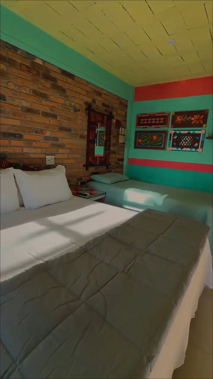 Quarto com cama queen, parede de tijolos e decoração colorida