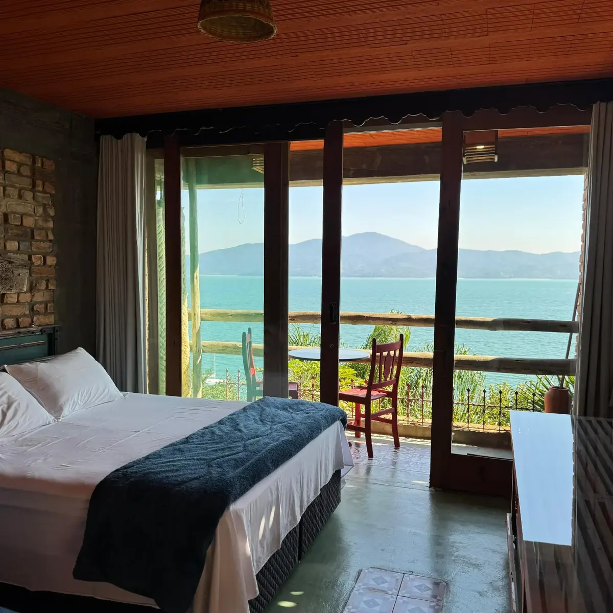 Quarto com cama de casal e porta de vidro para a varanda com vista do mar